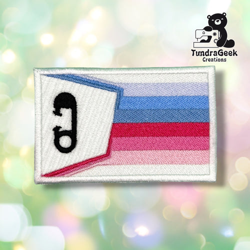 Front view of a rectangular white satin patch embroidered with a small waving ABDL pride flag graphic — light blue, blue, white, magenta, pink, and light pink horizontal stripes — with a black embroidered diaper pin icon on the flag's white fold.