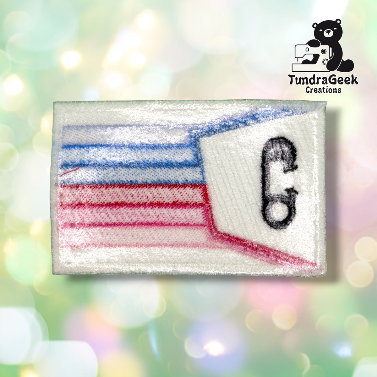 Back of the patch showing the reverse side of the embroidery, with the stripe colors and diaper pin outline visible in softer, blended thread color through the white backing.