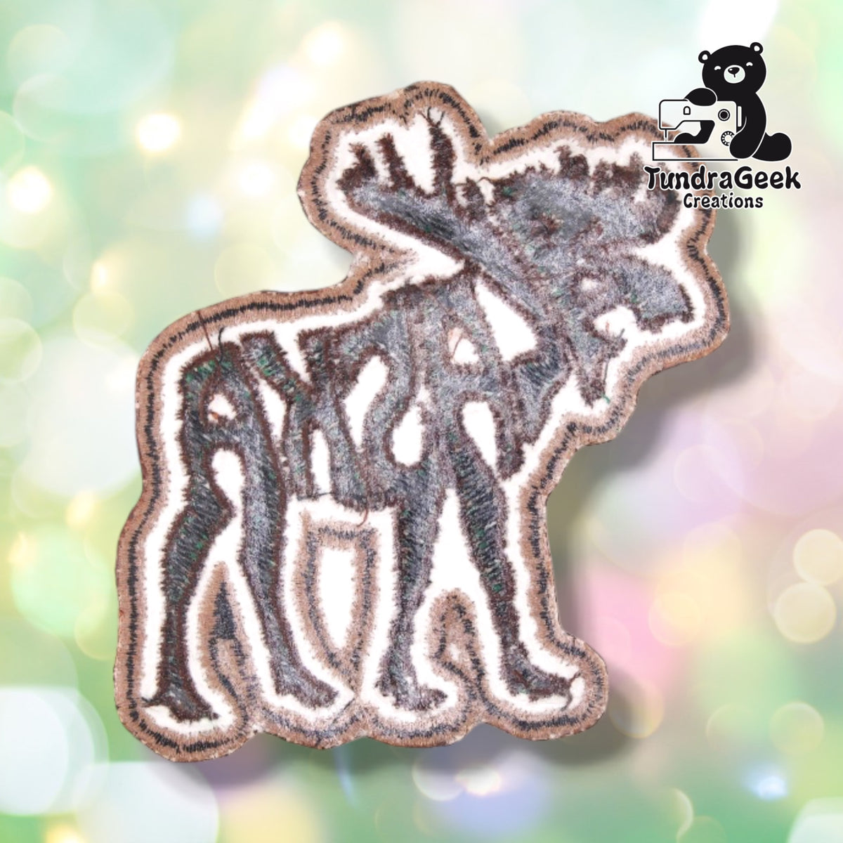 Back of the patch showing the reverse side of the embroidery in muted, softened colors, with the moose silhouette and lettering faintly visible and mirrored through the backing fabric.