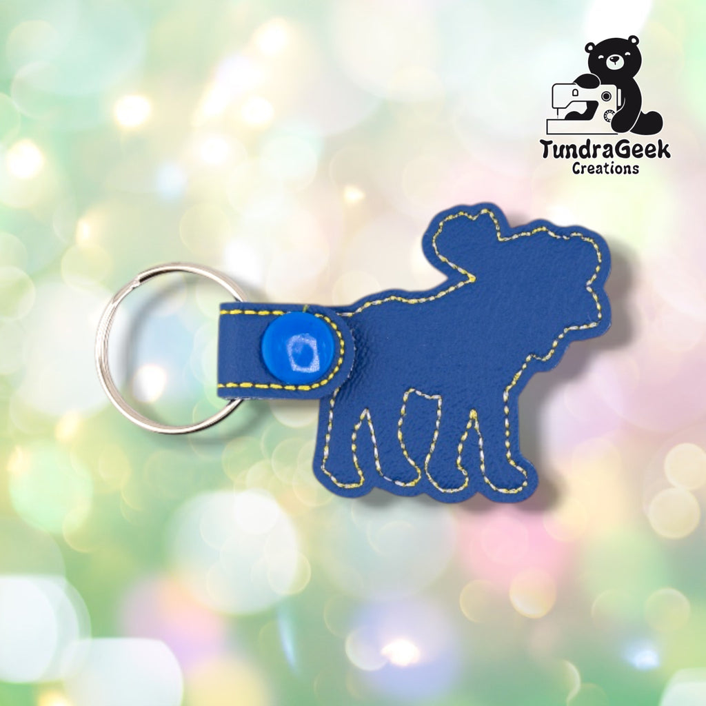 Back of the keychain, showing a plain blue vinyl reverse side with yellow and white outline stitching following the moose silhouette. Blue plastic snap closure and metal split ring at top.