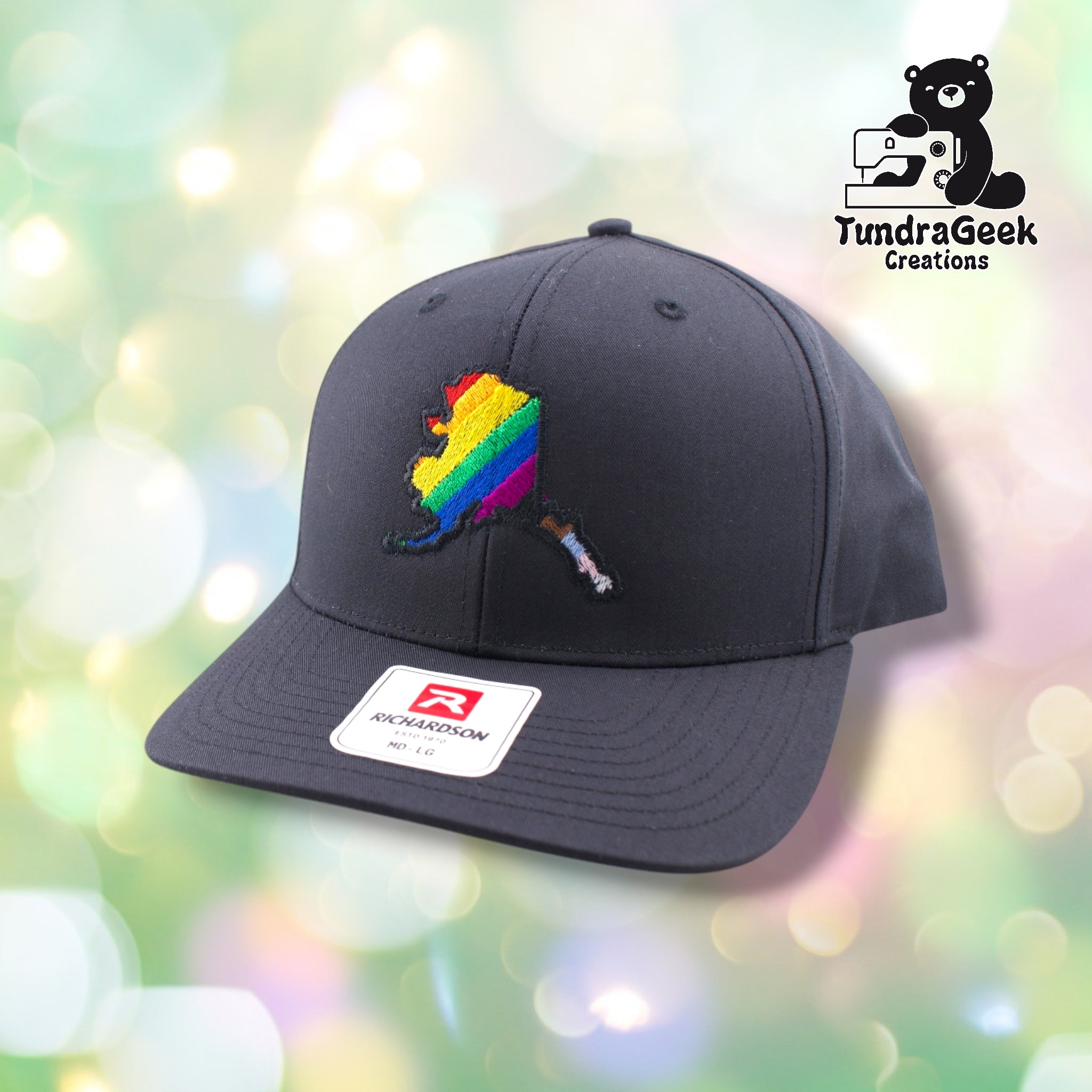 A black Richardson baseball cap with a colorful rainbow-striped Alaska state map embroidery and paintbrush design.