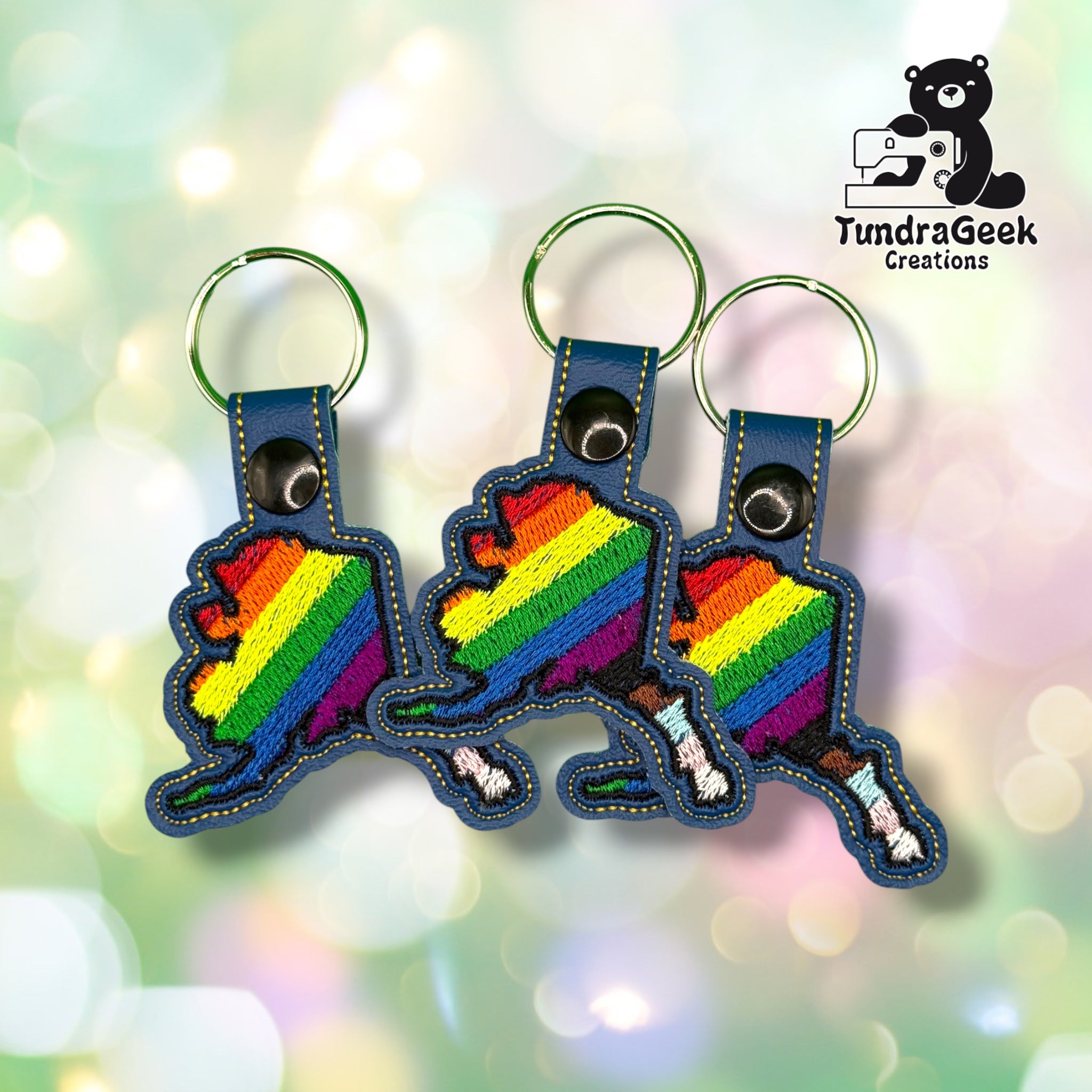 Three Alaska State Pride keychains grouped together, each showing the same rainbow-to-Progress-Pride Alaska state design on blue vinyl.