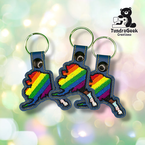 Three Alaska State Pride keychains grouped together, each showing the same rainbow-to-Progress-Pride Alaska state design on blue vinyl.