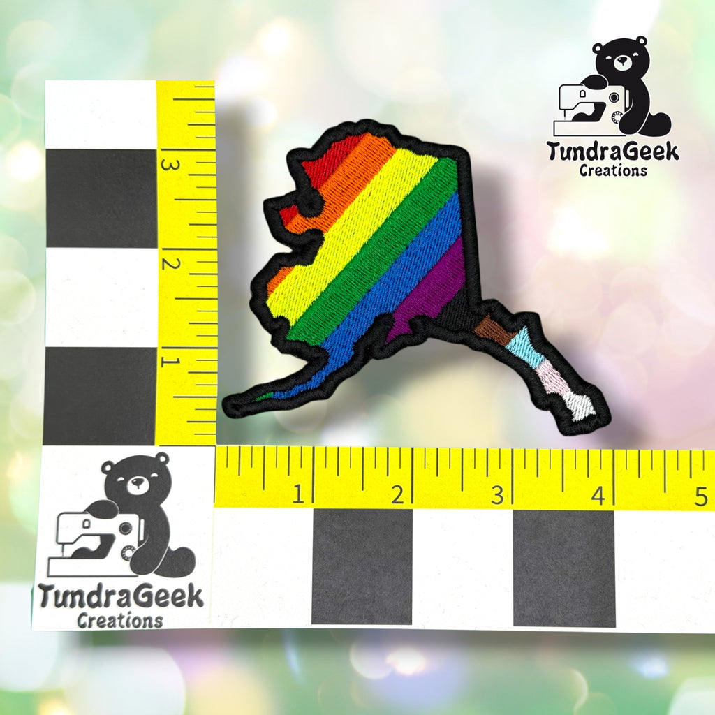 Patch shown against a black-and-white checkered background with yellow rulers for scale, measuring approximately 4 inches wide by 3.5 inches tall.  ---