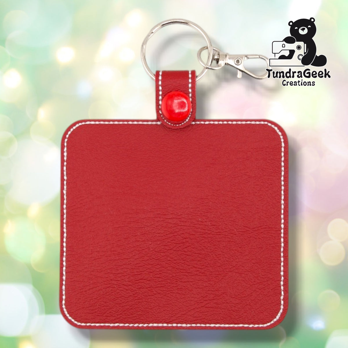 Back of the red badge, showing a plain reverse side with white outline stitching following the square shape. Silver lobster claw clip and red snap hardware at top.