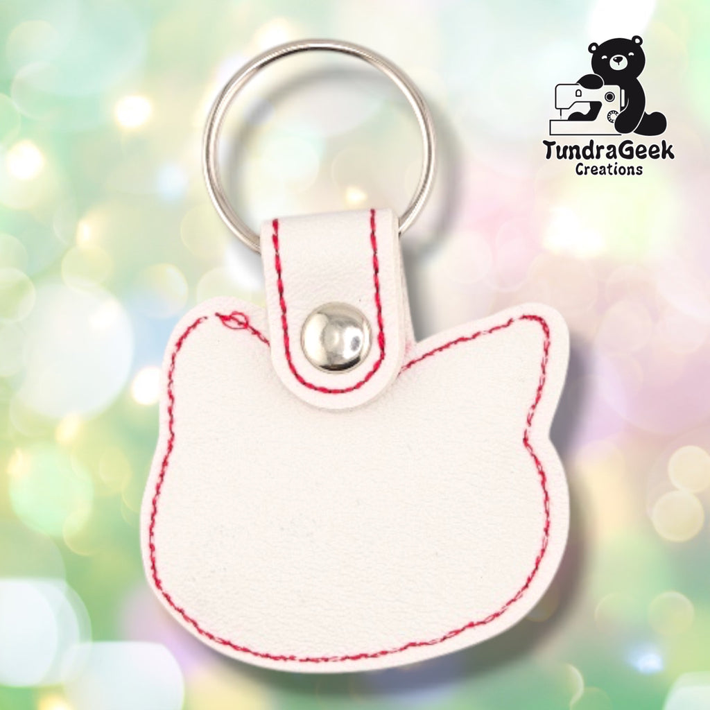 Back of the keychain, showing a plain cream vinyl reverse side with red outline stitching following the cat's head silhouette. Silver snap closure and metal split ring at top.