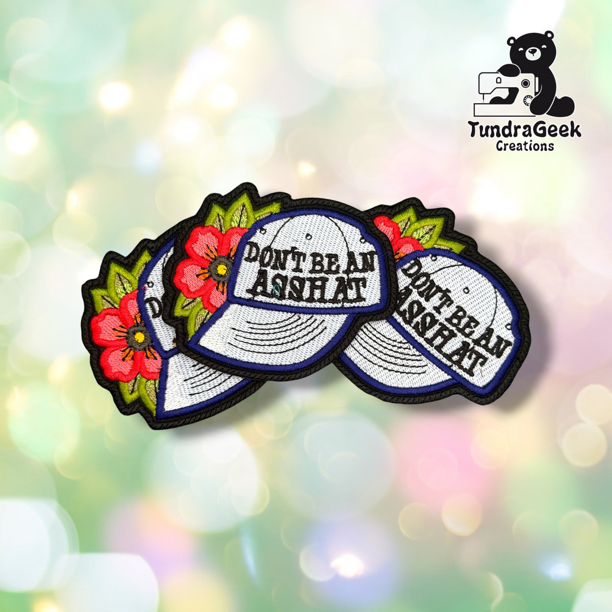Four "Don't Be an Asshat" patches fanned out together, each showing the same cap-and-floral design with navy merrowed edges.