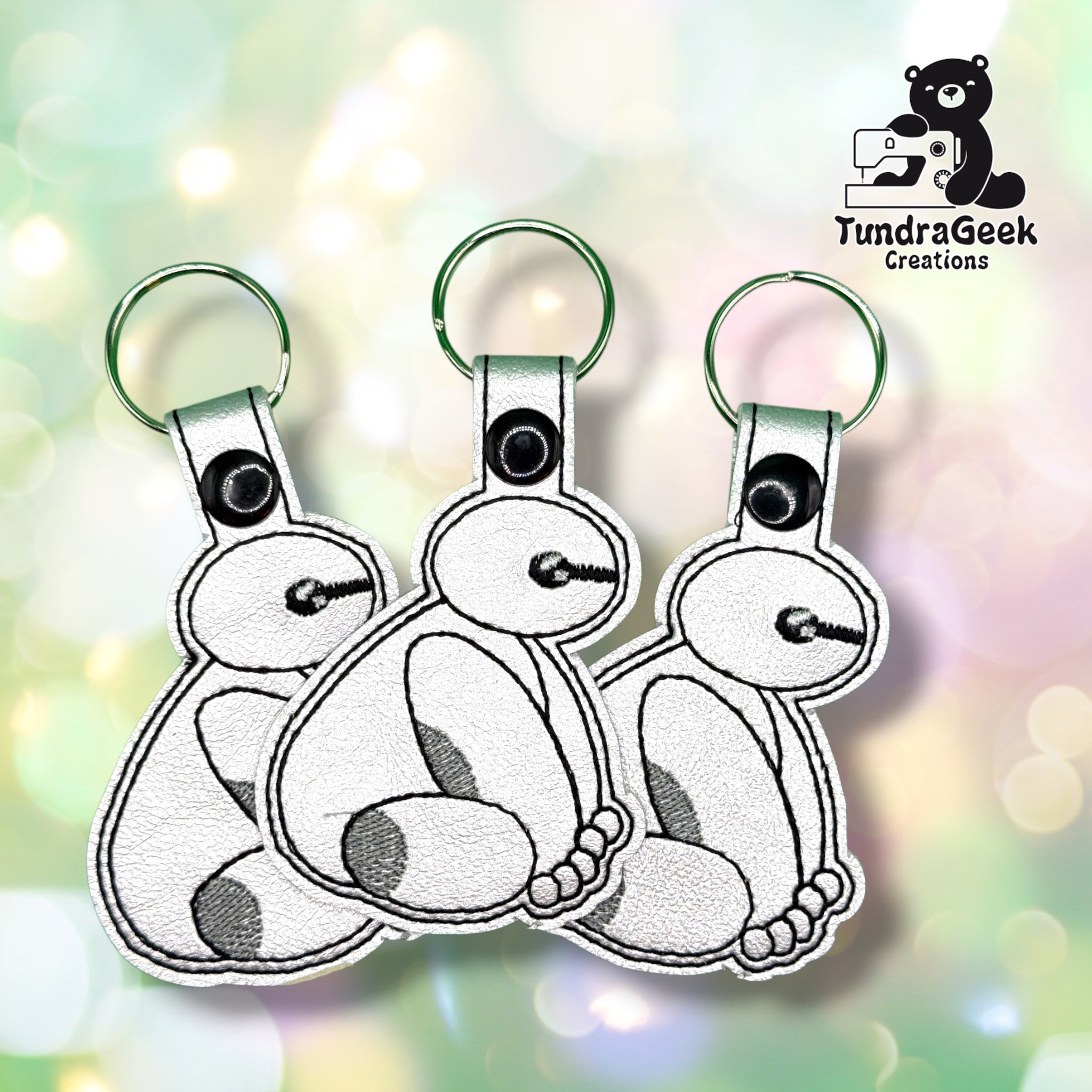 Three Balalalala keychains fanned out together, each showing the same seated robot-companion design with grey shading and a black ball-tipped wand.