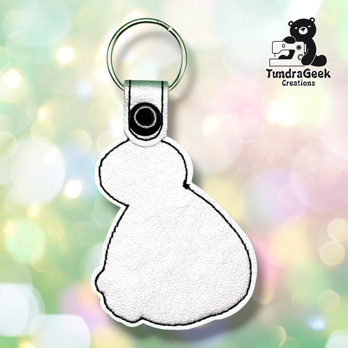 Back of the keychain showing the plain white vinyl backing with a black stitched outline, black plastic snap closure, and green split ring. No embroidery visible from this side.