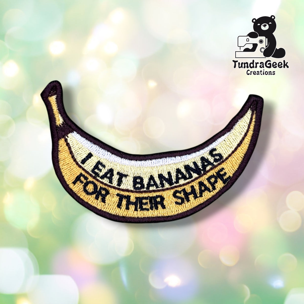 Front view of a banana-shaped patch embroidered in yellow, white, and brown, with "I EAT BANANAS FOR THEIR SHAPE" stitched in black block lettering along the curve of the banana.