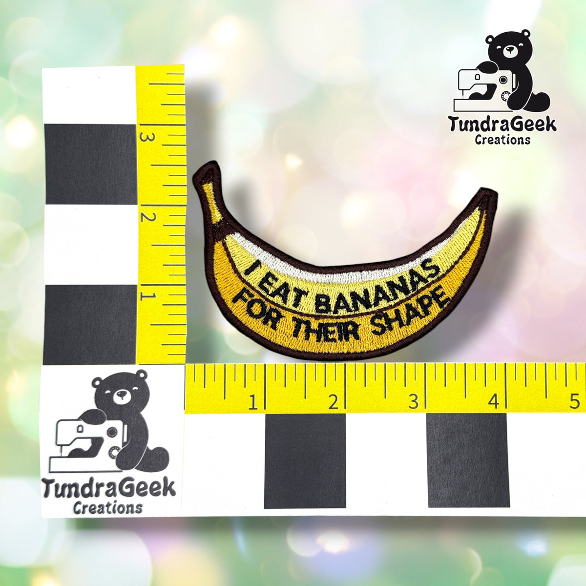 Patch shown against a black-and-white checkered background with yellow rulers for scale, measuring approximately 4 inches long by 2.5 inches tall.  ---