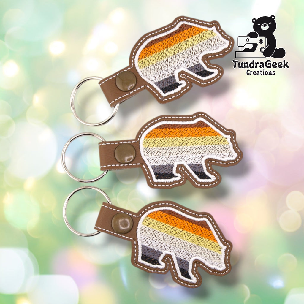 Three identical Bear-Shaped Bear Pride keychains fanned out together, each showing the same flag-striped bear silhouette.