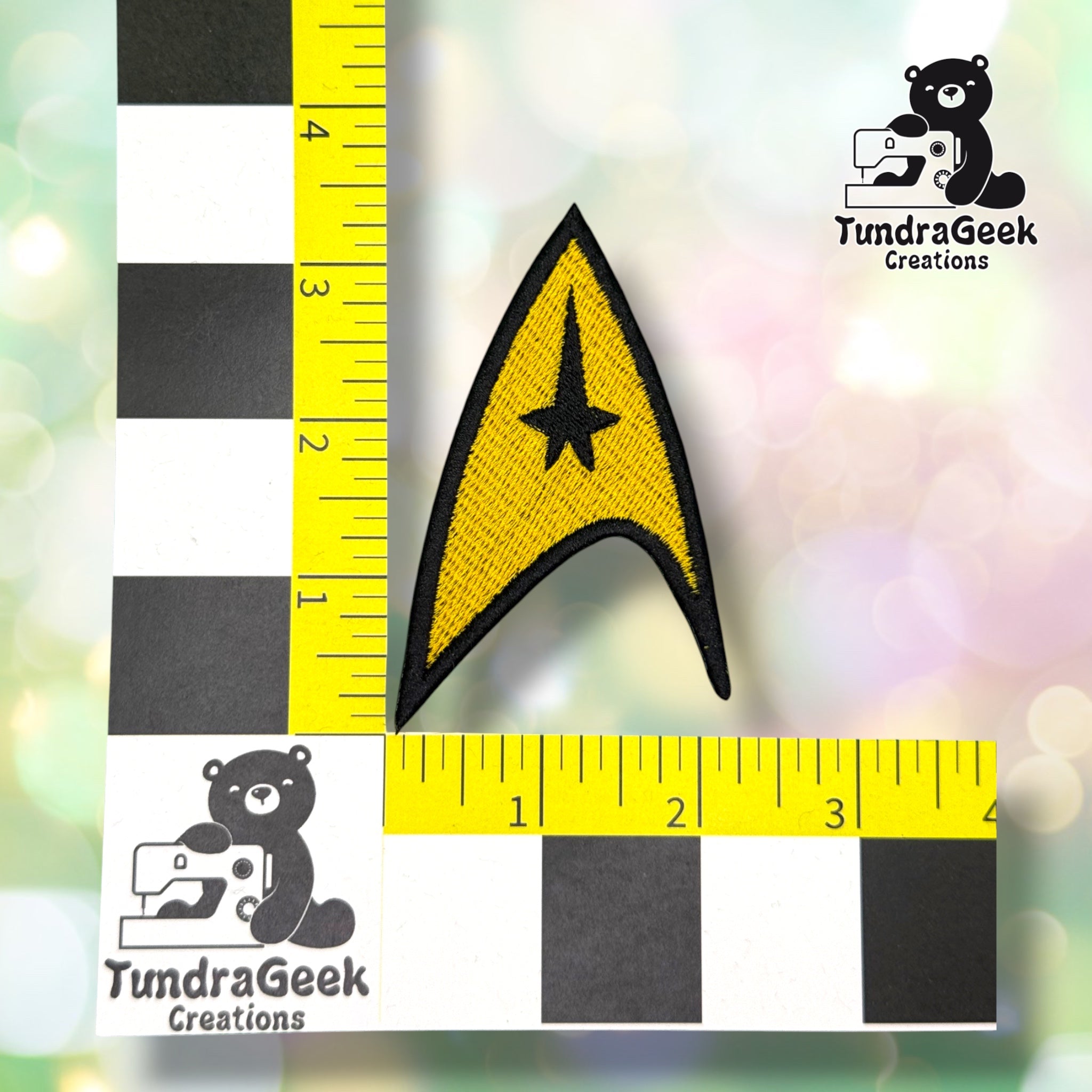 A gold and black arrowhead-shaped embroidered patch with a star motif, shown next to a ruler measuring approximately 3.5 inches. TundraGeek Creations logo in the top right corner.