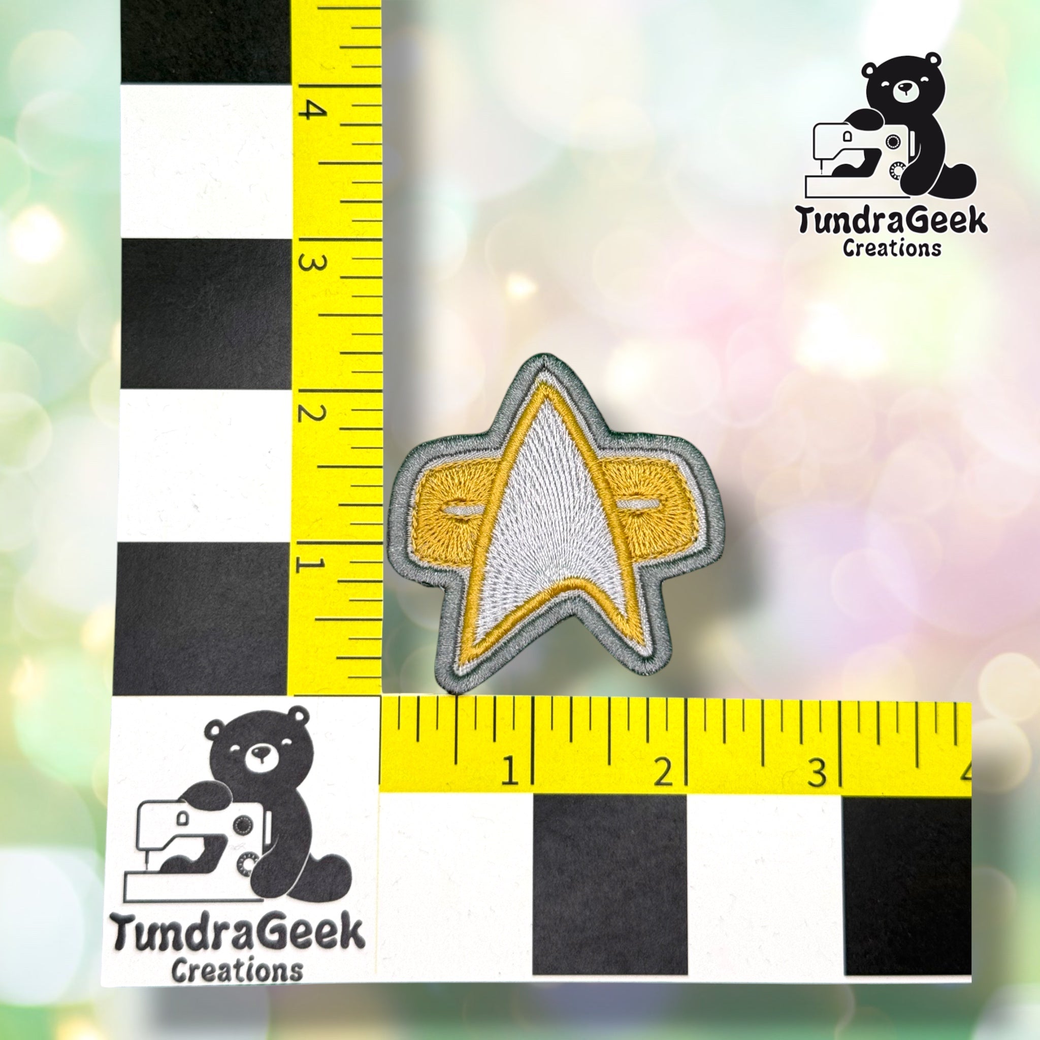A silver and gold star-shaped embroidered patch, shown next to a ruler measuring approximately 2.5 inches. TundraGeek Creations logo in the top right corner.