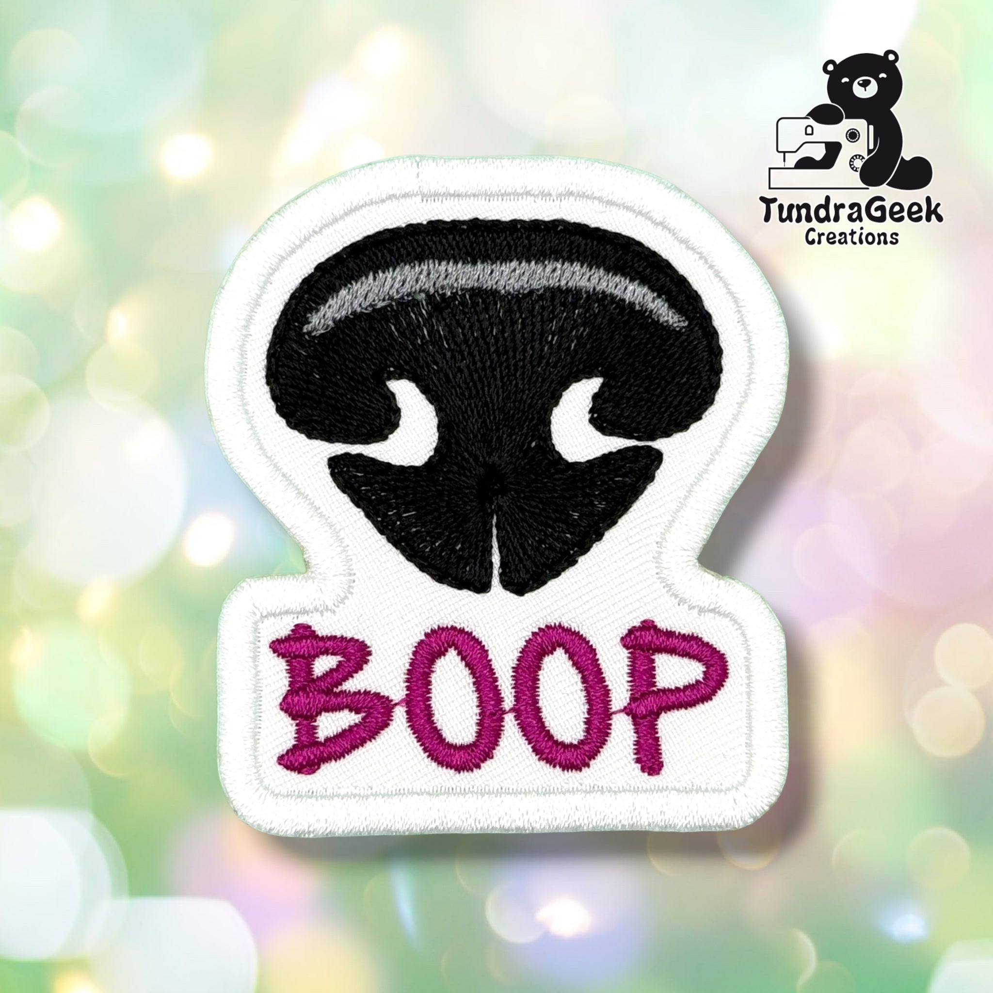 Front view of a white patch embroidered with a black dog nose featuring a grey highlight stripe, with "BOOP" stitched below in magenta script lettering.