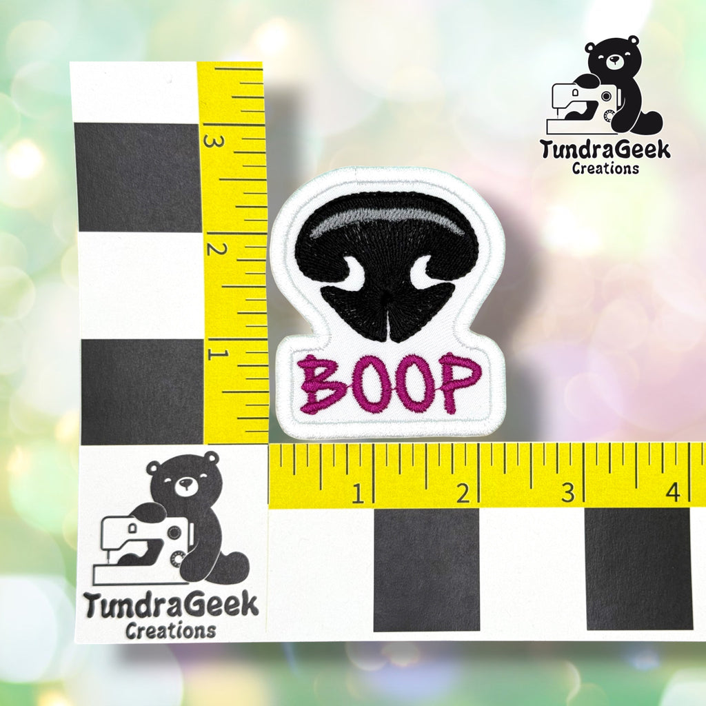 Patch shown against a black-and-white checkered background with yellow rulers for scale, measuring approximately 2.25 inches wide by 2.5 inches tall.  ---