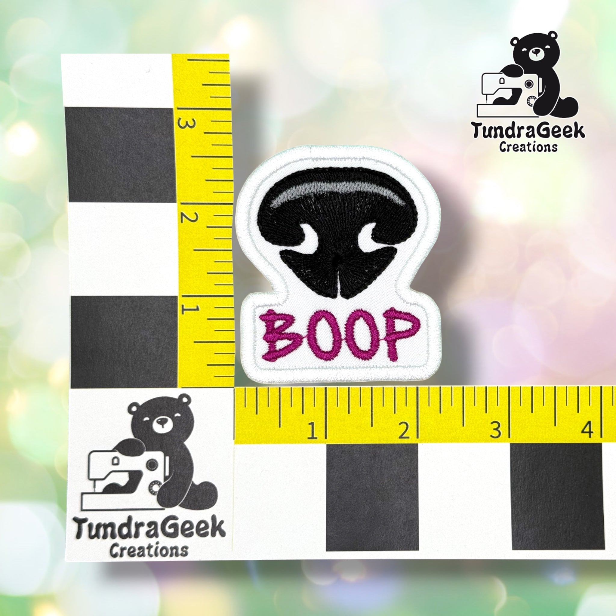 Patch shown against a black-and-white checkered background with yellow rulers for scale, measuring approximately 2.25 inches wide by 2.5 inches tall.  ---