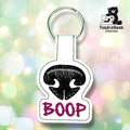 Front view of a white vinyl keychain embroidered with a black dog nose featuring a grey highlight stripe, with "BOOP" stitched below in magenta lettering. Finished with a white plastic snap closure and green split ring.
