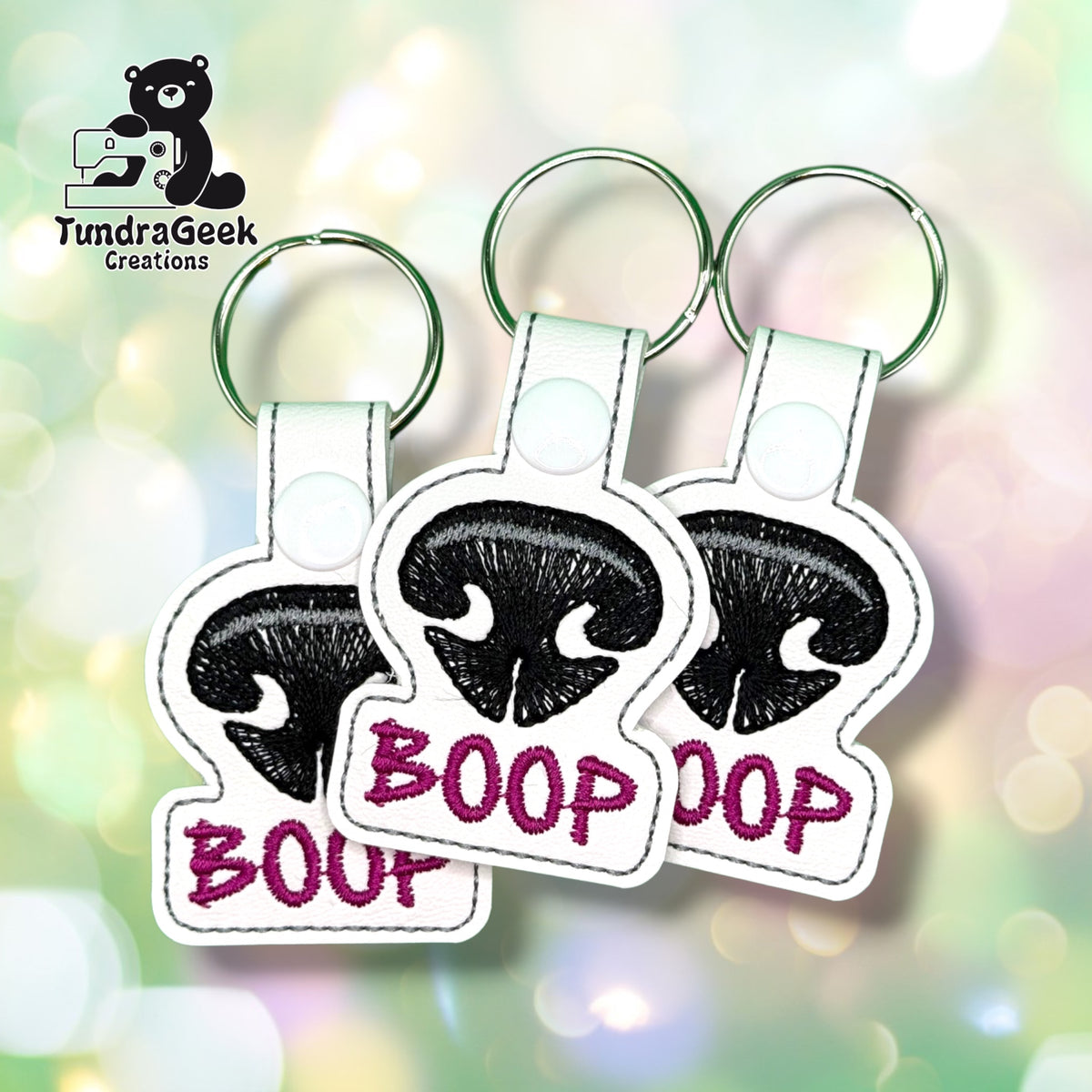 Three Dog Nose Boop keychains fanned out together, each showing the same black nose design with magenta "BOOP" lettering on white vinyl.