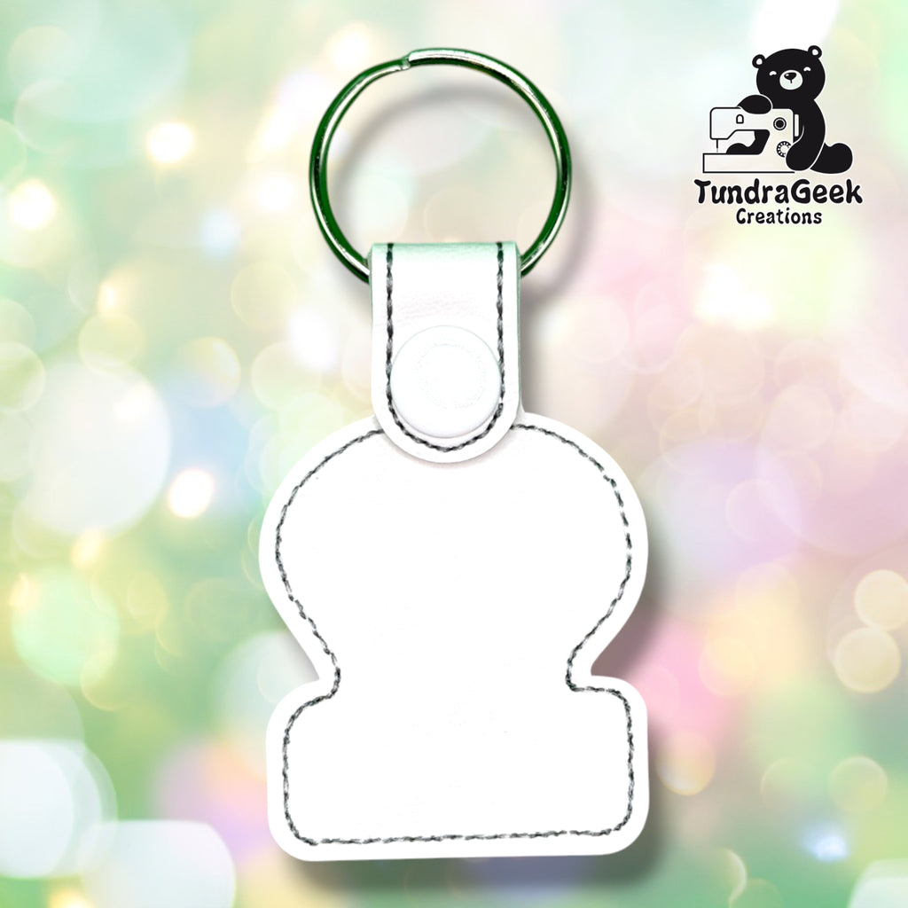 Back of the keychain showing the plain white vinyl backing with a grey stitched outline, white plastic snap closure, and green split ring. No embroidery visible from this side.