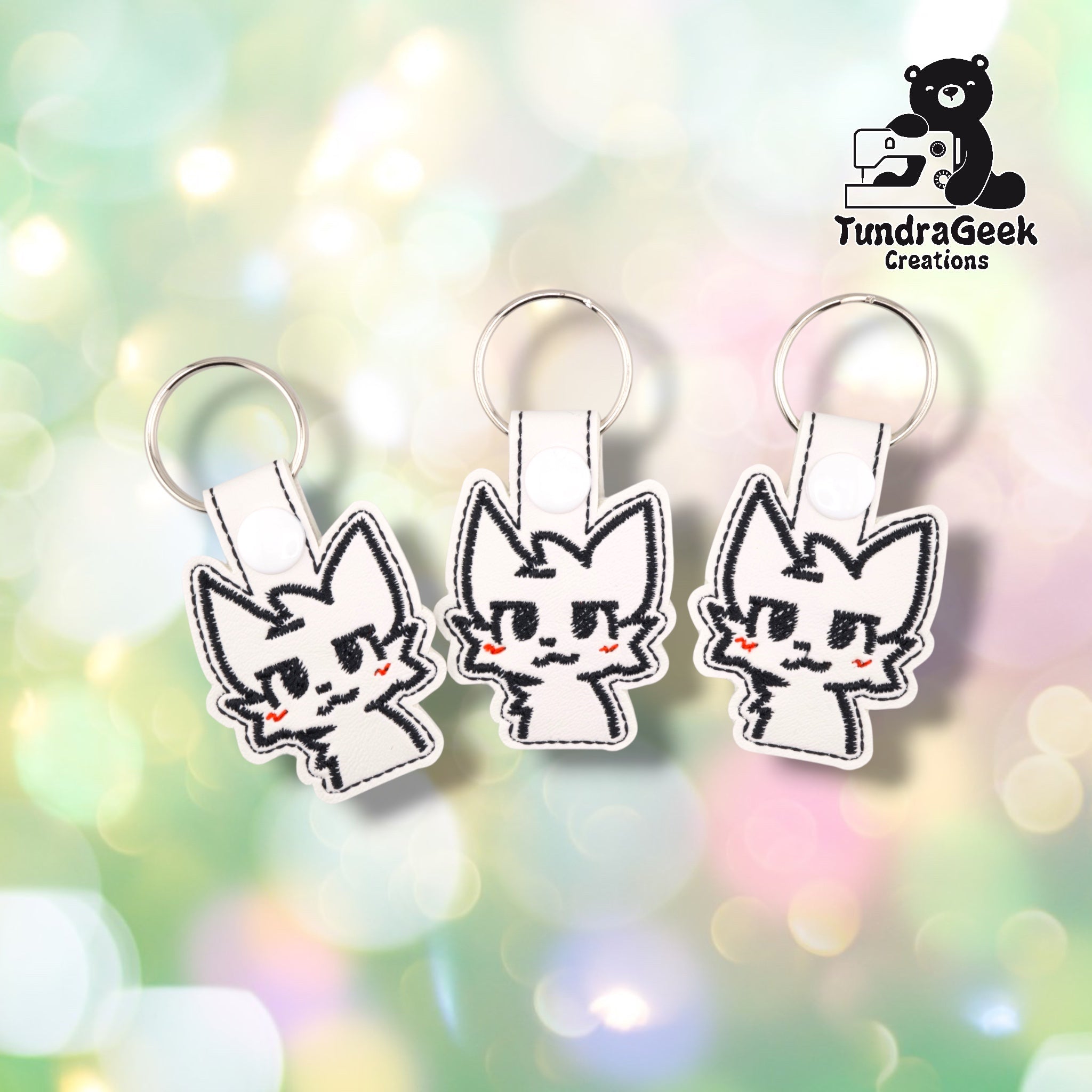 Three Boykisser keychains grouped together against a soft bokeh background, each on white faux leather vinyl with the same black-stitched cat face design and matching red zigzag cheek accents, showing the slight natural variation between handmade units.