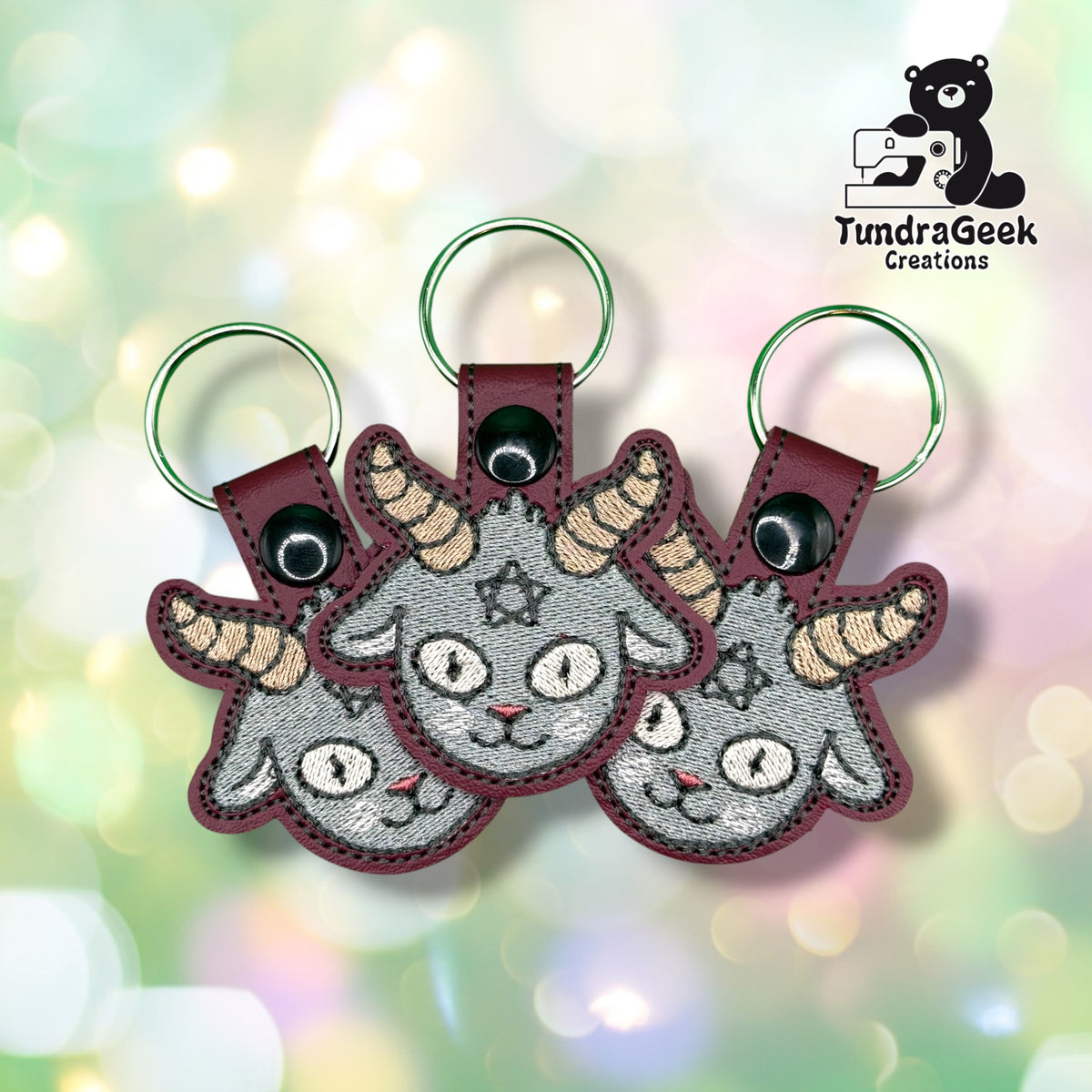 Three Cheeky Baphomet keychains fanned out together, each showing the same grey goat face design with striped horns and a small star between the brows.