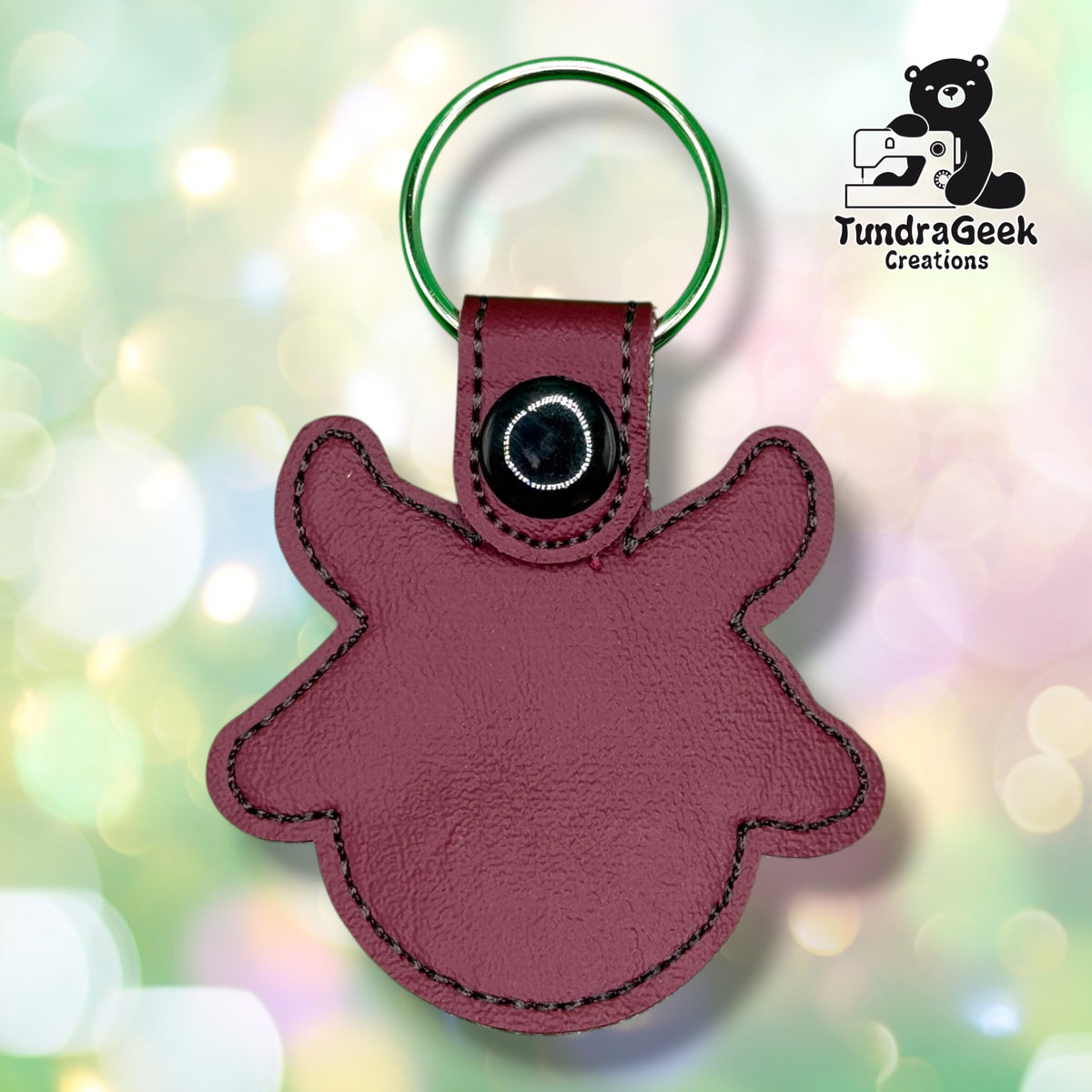 Back of the keychain showing the plain maroon vinyl backing with a grey stitched outline, black plastic snap closure, and green split ring. No embroidery visible from this side.