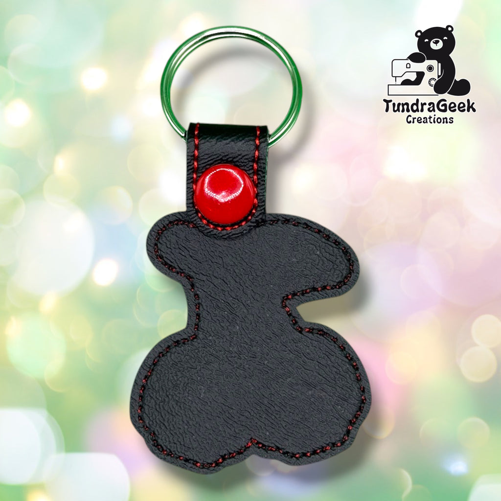 Back view of the keychain showing the plain black vinyl backing with red stitched edge detailing, a red plastic snap closure tab, and a green split ring. No embroidery visible from this side.