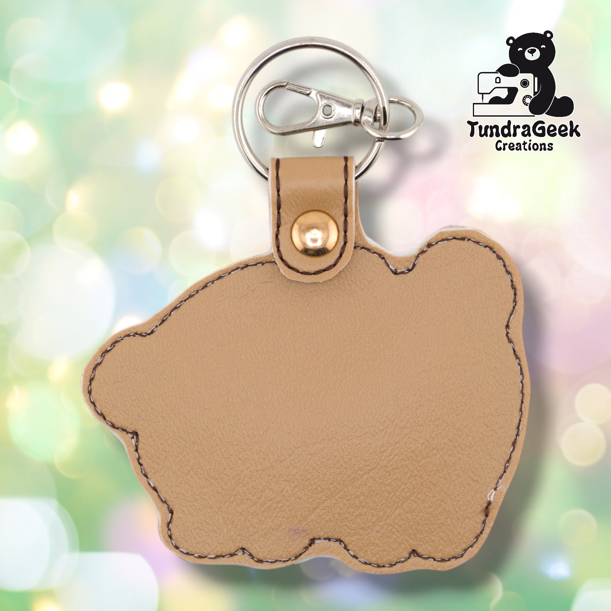 The reverse side of the chubby pug keychain, showing a plain tan vinyl back in the same rounded pug body silhouette shape. Dark brown edge stitching follows the outline. Gold snap hardware and silver lobster claw clip with split ring at top.
