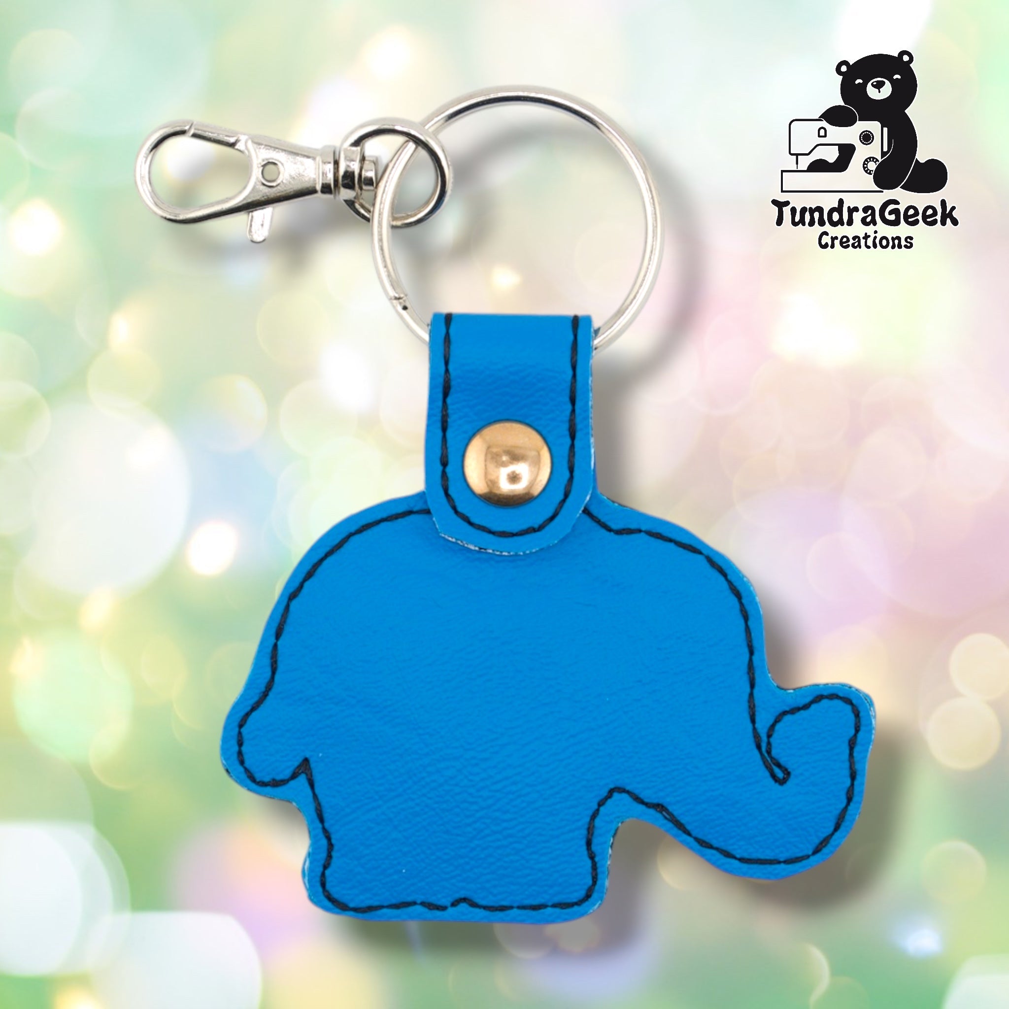 The reverse side of the circus elephant keychain, showing a plain bright blue vinyl back in the same elephant silhouette shape. Black edge stitching follows the outline of the head, body, trunk, and legs. Gold snap hardware and silver lobster claw clip with split ring at top.