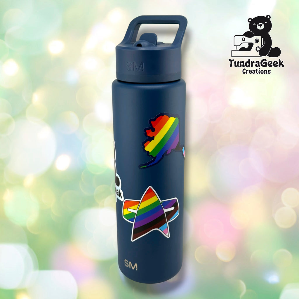 Navy steel water bottle with the delta badge pride sticker and a rainbow Alaska-shaped sticker applied to the side, showing real-world placement.