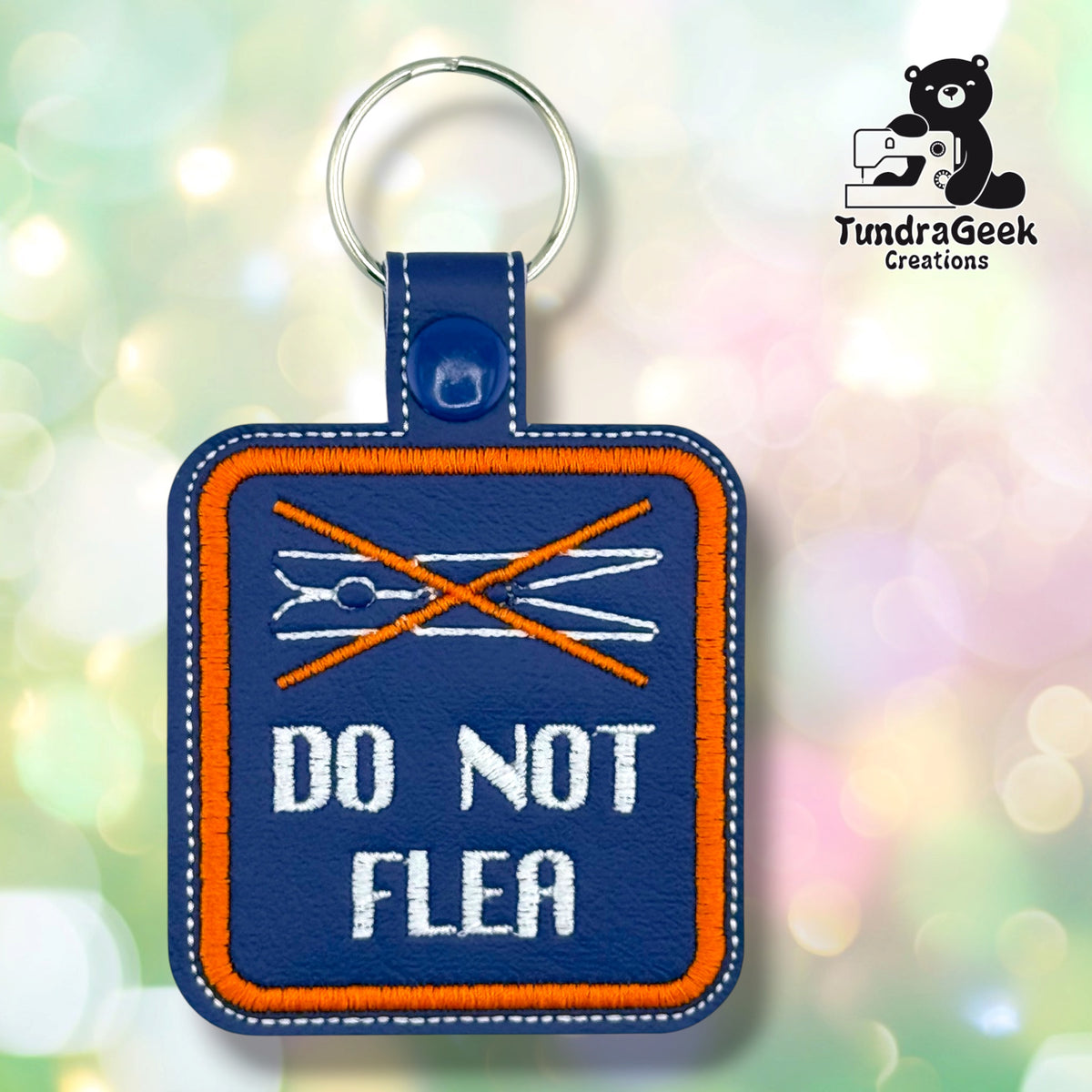 Purple embroidered vinyl keychain badge reading “DO NOT FLEA” in white text beneath a white line-art clothespin crossed out with an orange X. An orange border stitched around the design and white topstitching along the edge. A blue plastic snap closes the tab around a silver split ring; the lobster claw clip that ships with the badge is not attached in this photo.