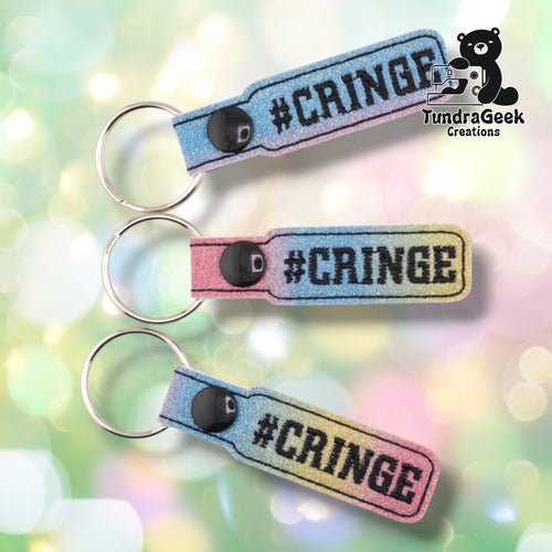 Three glittery keychain straps with #CRINGE text in gradient colors of blue, pink, and yellow against a soft blurred background.