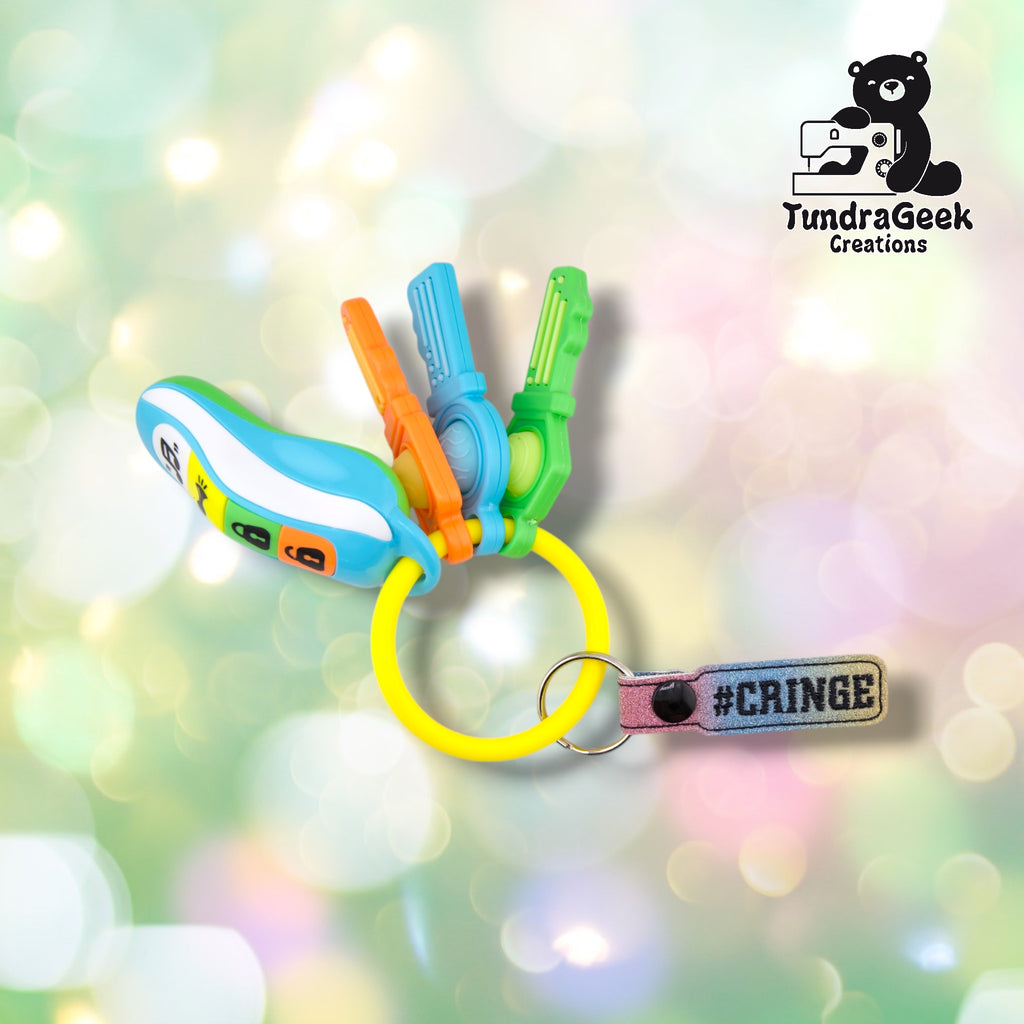 A colorful silicone keychain featuring a blue and white curved band, three hanging toy tools in orange, blue, and green, a yellow ring, and a pink #CRINGE tag.