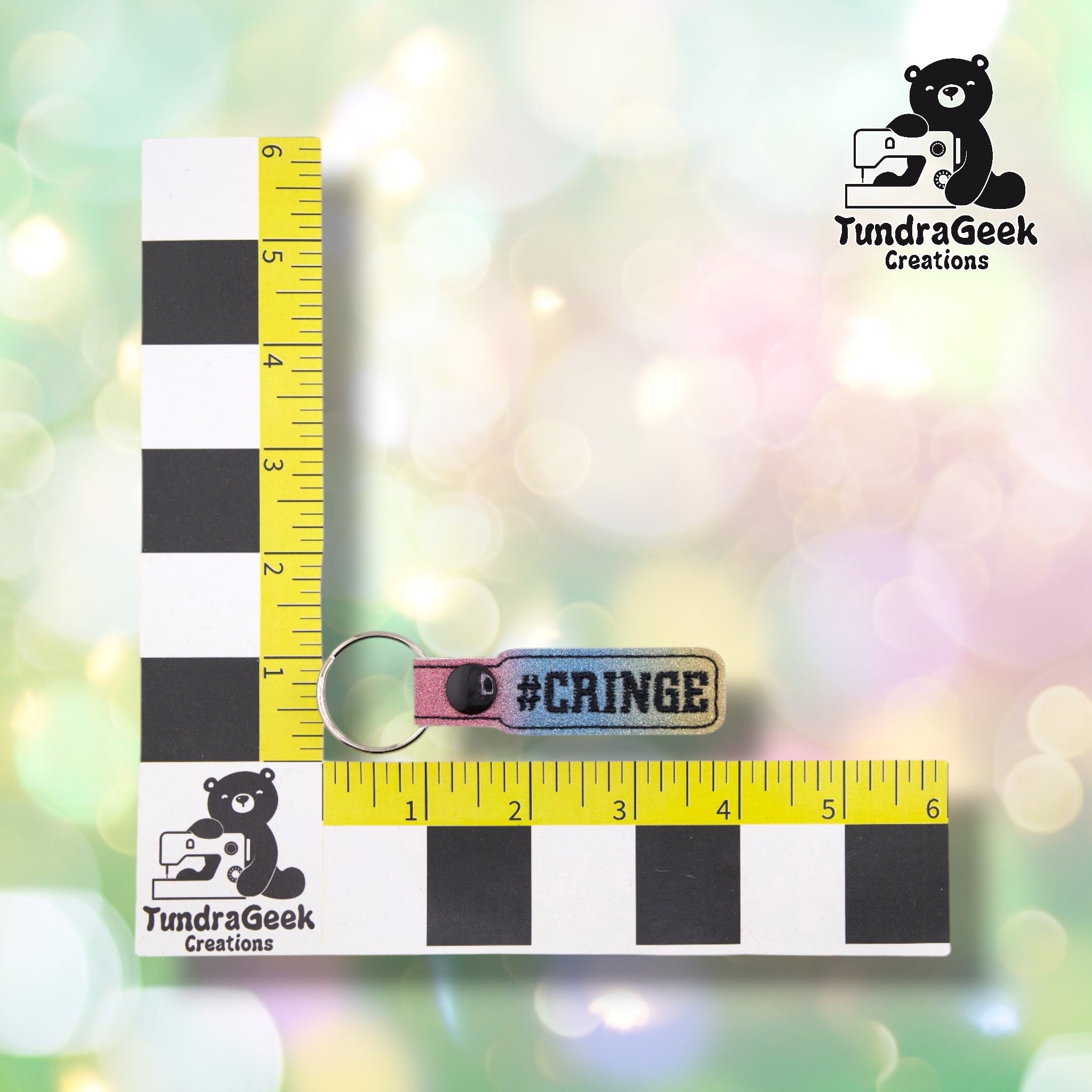 A pink and blue ombre keychain with "#CRINGE" text displayed on a yellow measuring tape next to TundraGeek Creations branding.