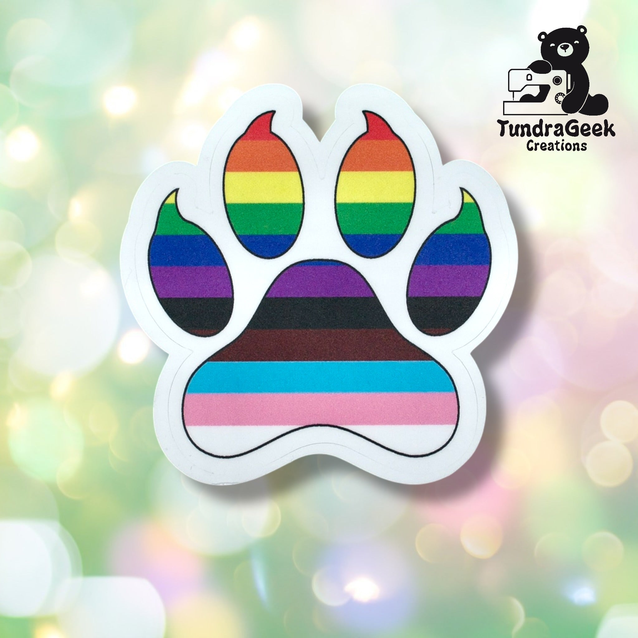 A paw print sticker featuring multiple LGBTQ+ pride flag colors on a blurred, pastel background with the TundraGeek Creations logo in the top right corner.