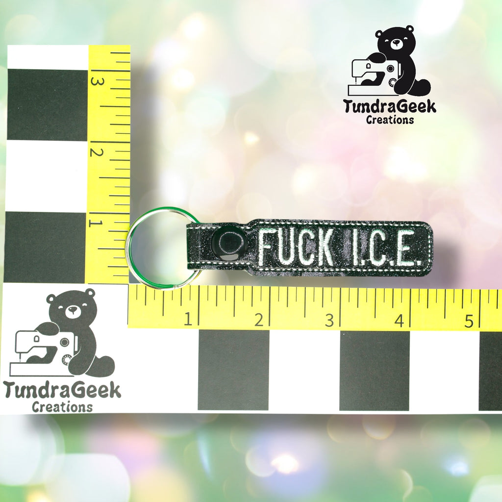 A keychain reading FUCK I.C.E. is placed on a ruler grid with TundraGeek Creations logo in the background. The keychain measures approximately 4 inches long.