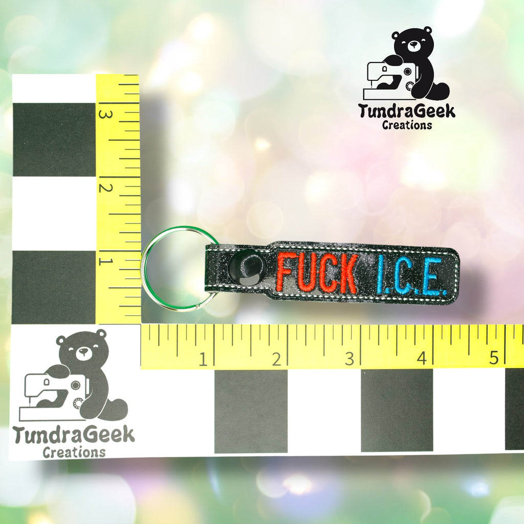 Keychain with embroidered text FUCK I.C.E. in red and blue letters, shown next to rulers for scale, with TundraGeek Creations logo in the background.