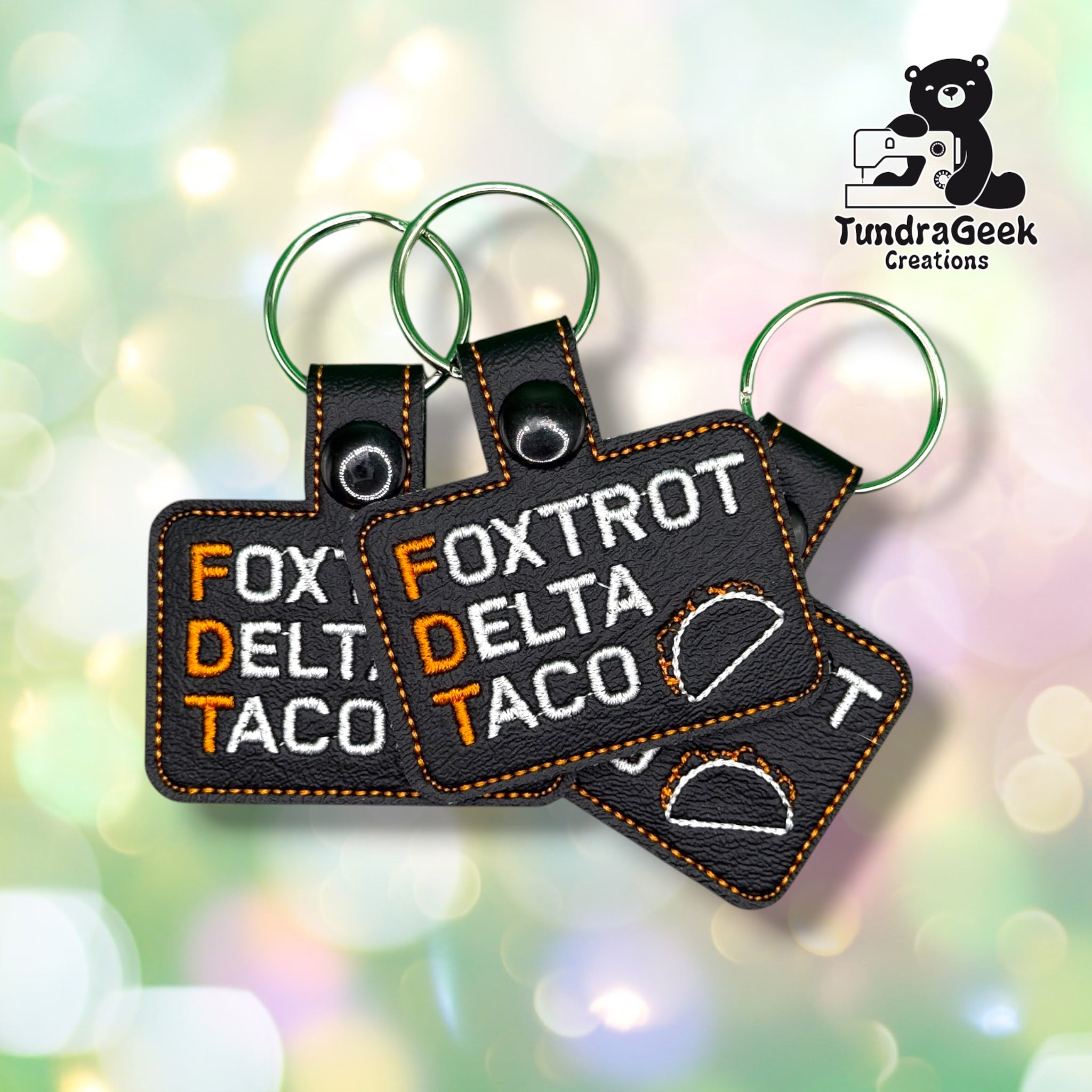 Three FDTaco keychains fanned out together, each showing the same "FOXTROT DELTA TACO" lettering and taco outline design.
