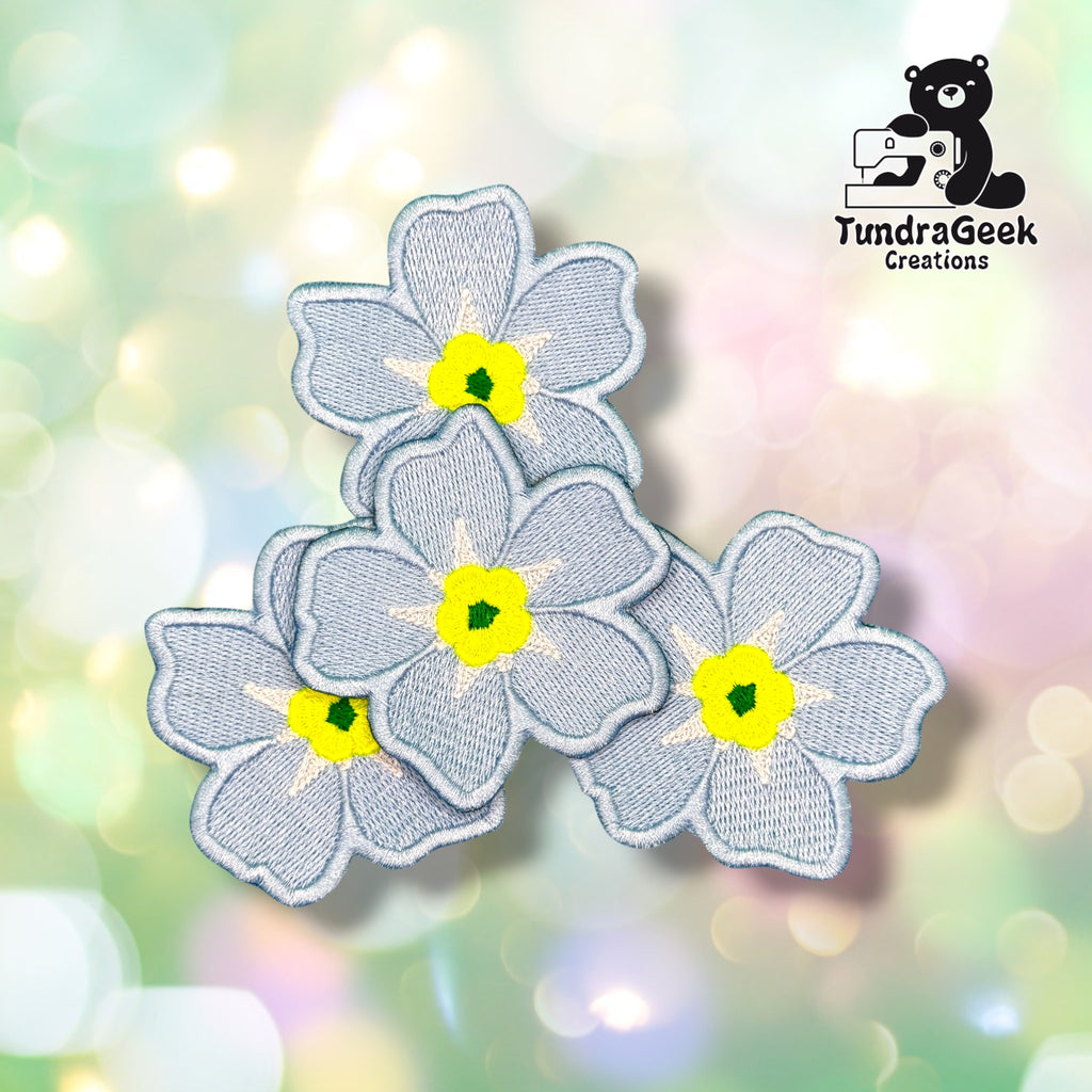 Three Forget-Me-Not patches grouped together, each showing the same soft blue five-petaled flower design with a yellow center.