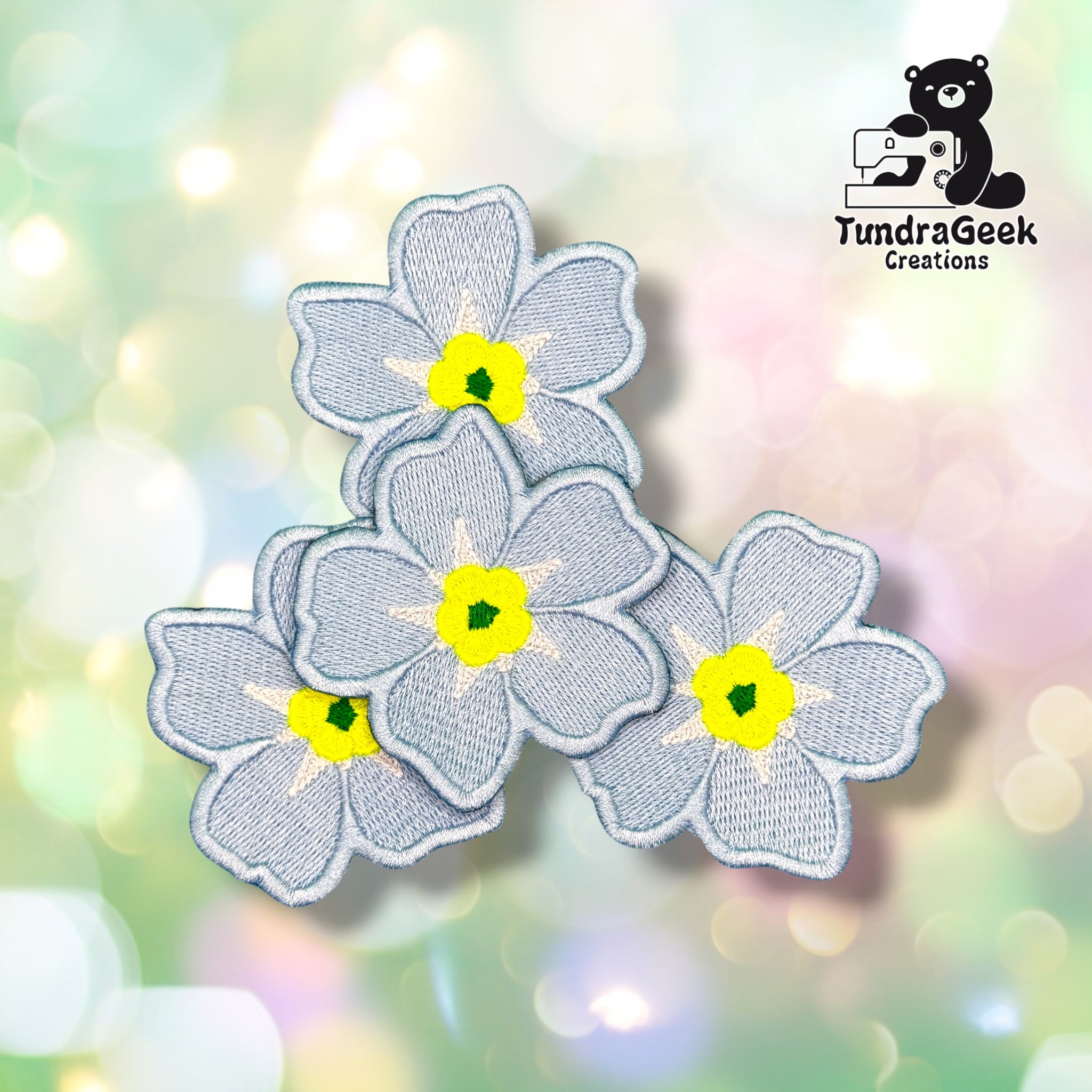 Three Forget-Me-Not patches grouped together, each showing the same soft blue five-petaled flower design with a yellow center.