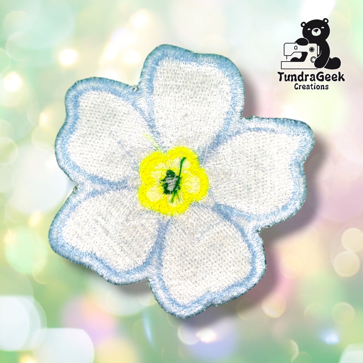 Back of the patch showing the reverse side of the embroidery in white and pale thread, with the petal shapes and center faintly visible through the backing.