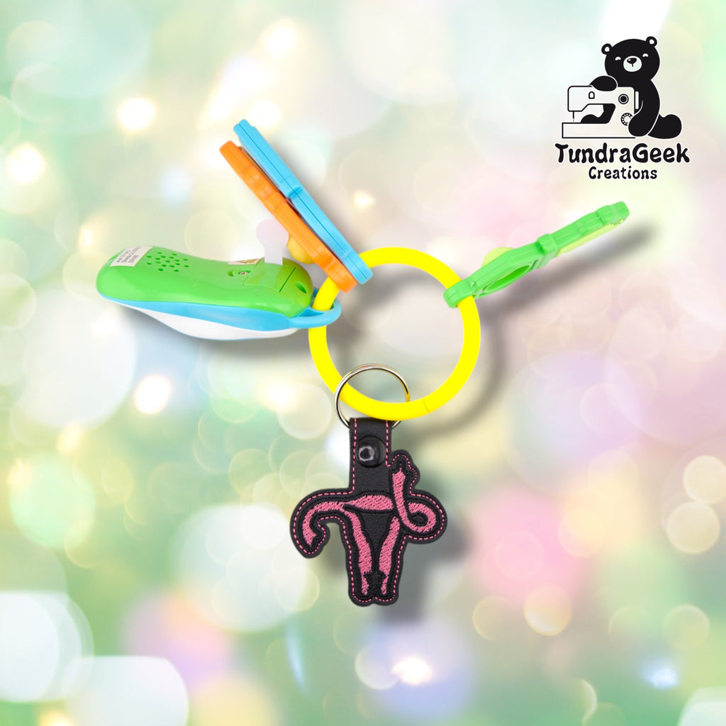 The black colorway clipped to a yellow silicone bangle keyring alongside a set of colorful plastic toy keys, showing the keychain in everyday use.  ---