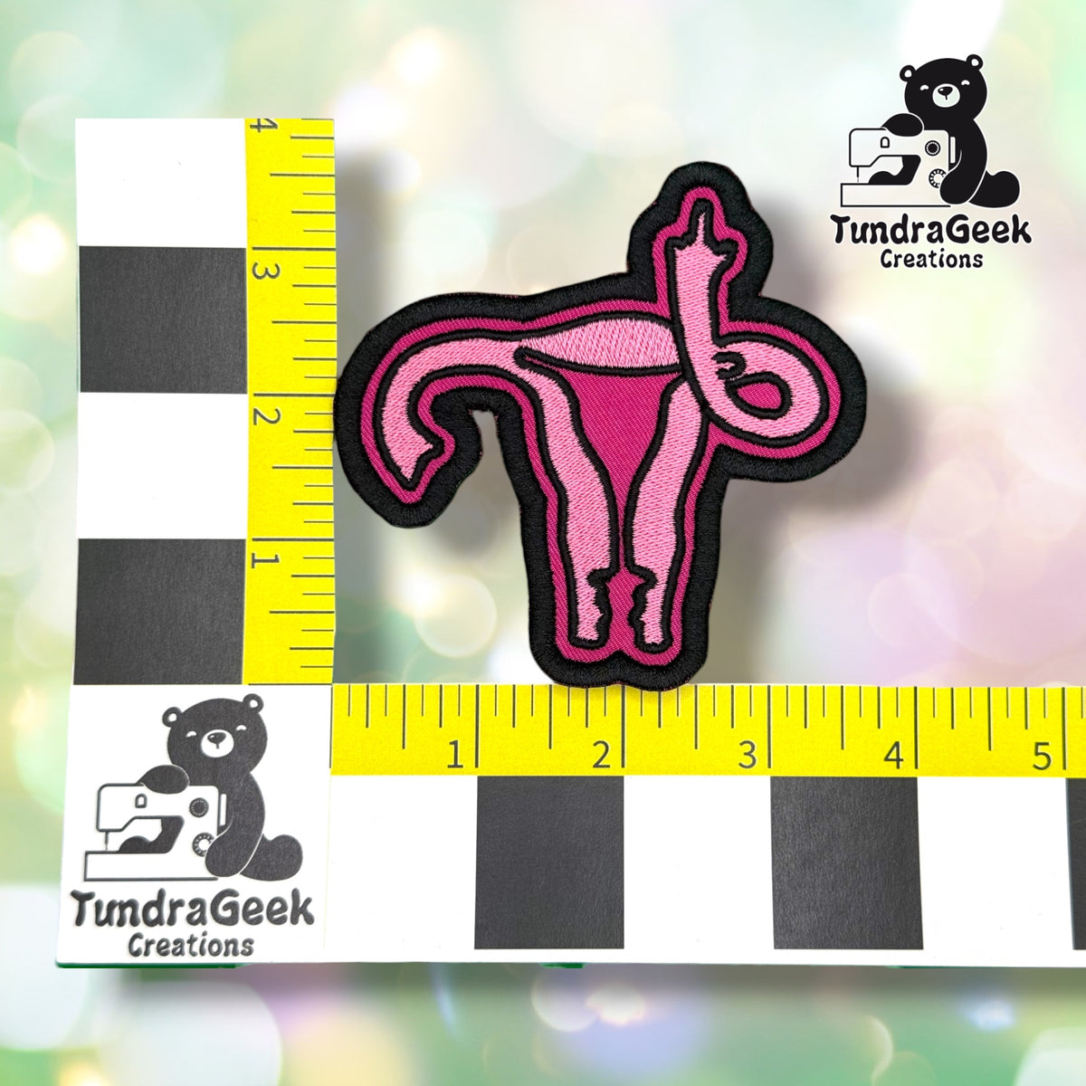 Patch shown against a black-and-white checkered background with yellow rulers for scale, measuring approximately 4 inches by 4 inches.  ---