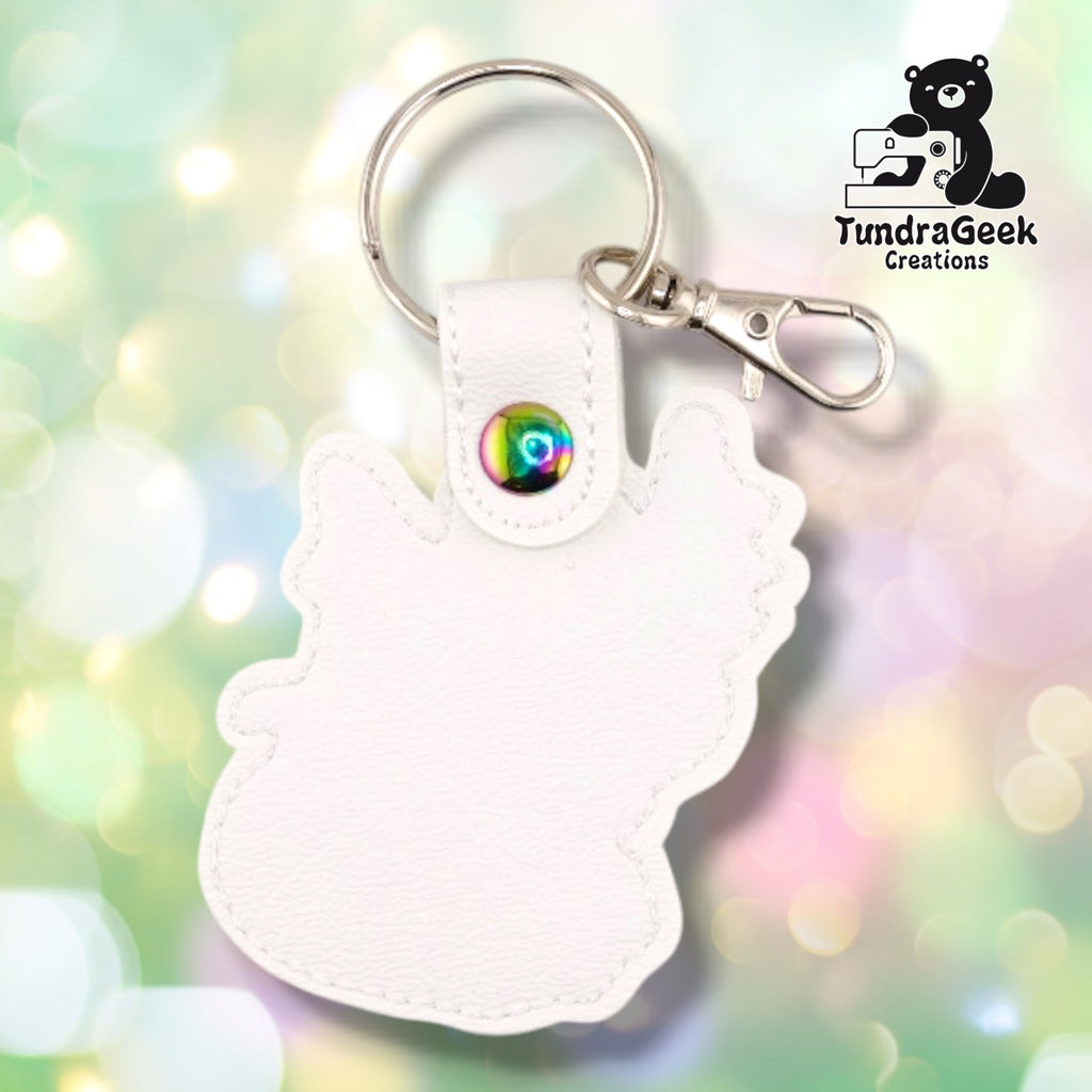 The back of the Femme Dragon keychain, showing plain white faux leather with no embroidery and the stitched outline following the dragon's silhouette. The snap tab is closed with an iridescent rainbow snap, with the split ring and silver swivel lobster clasp above it.