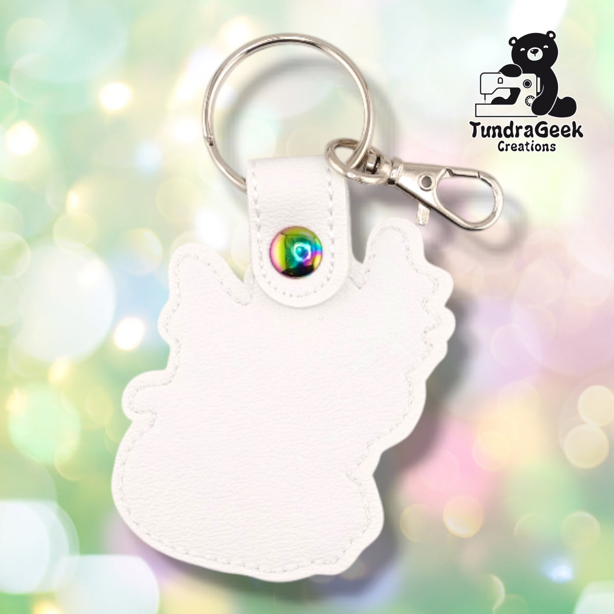 The back of the Femme Dragon keychain, showing plain white faux leather with no embroidery and the stitched outline following the dragon's silhouette. The snap tab is closed with an iridescent rainbow snap, with the split ring and silver swivel lobster clasp above it.