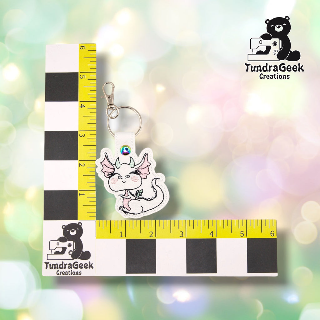 The Femme Dragon keychain photographed beside a yellow ruler marked in inches along both edges, for size reference. The keychain measures 3.75 inches tall by 2.5 inches wide including hardware.  ---