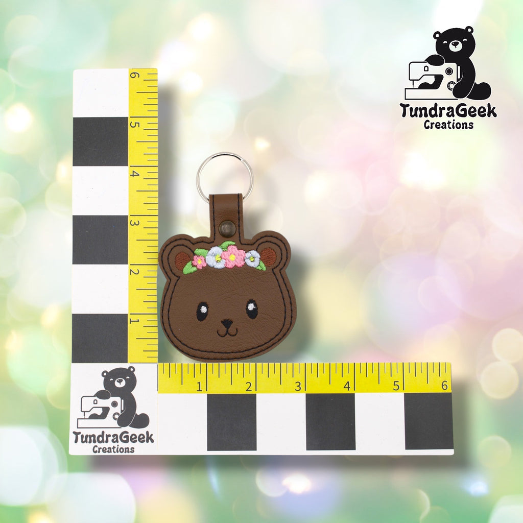 Brown floral bear keychain shown against a TundraGeek Creations L-shaped ruler prop. The keychain body measures approximately 3 inches wide by 2.75 inches tall. Total height including tab and split ring is approximately 4.25 inches.