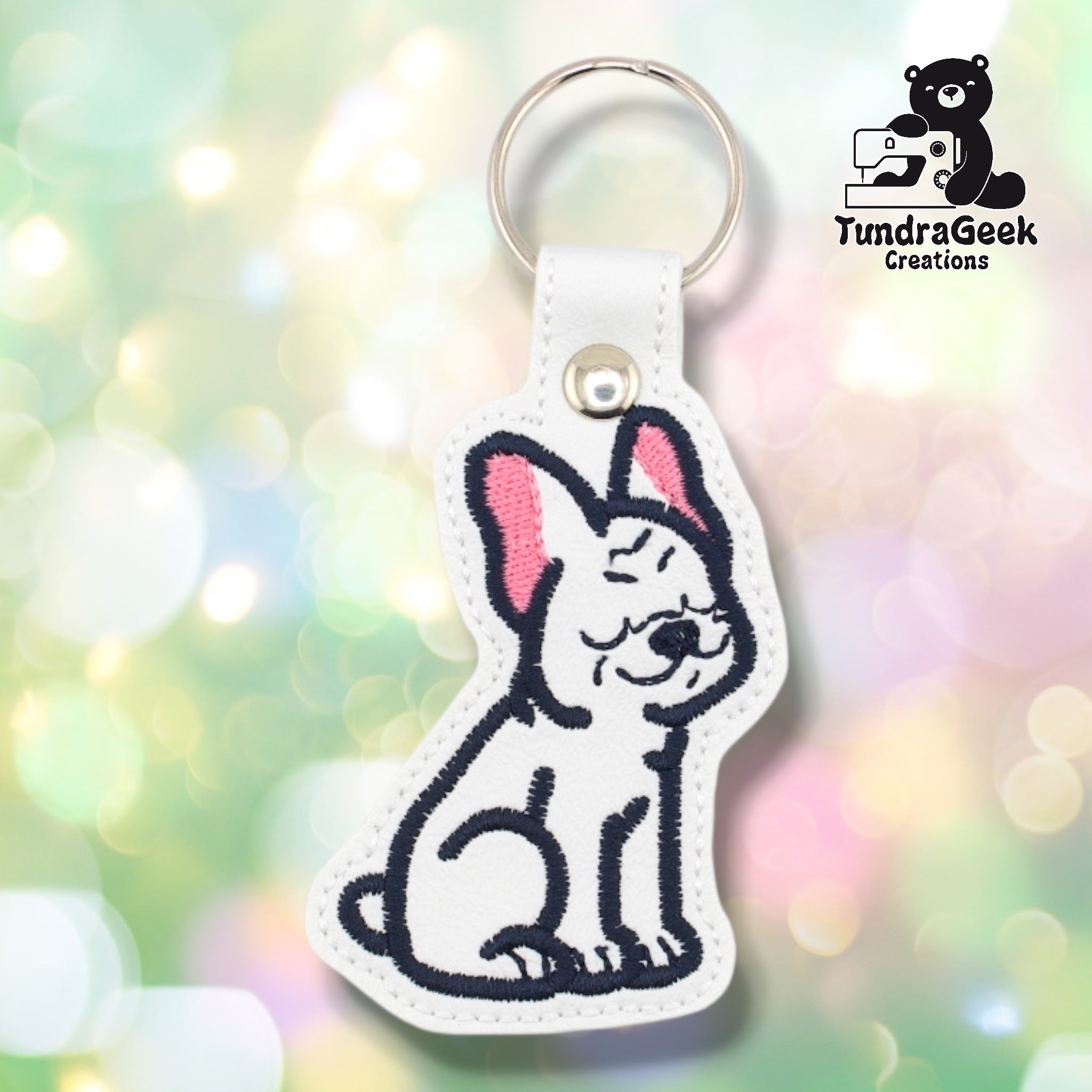 Front of a white faux leather French Bulldog keychain. An embroidered French Bulldog sits upright on a white vinyl base with pink inner ear accents and navy outline and facial detail stitching. A silver 9mm metal rivet closure is visible on the tab, with a silver split ring above.