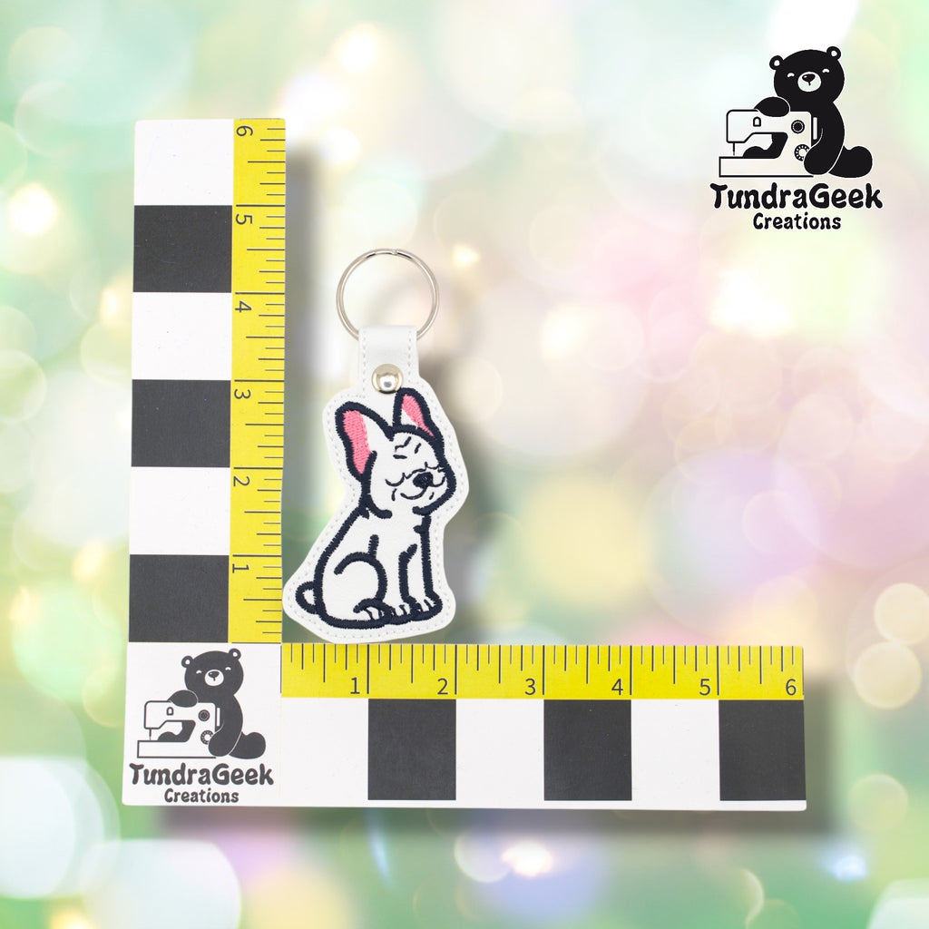 White French Bulldog keychain shown against a TundraGeek Creations L-shaped ruler prop. The keychain body measures approximately 2.125 inches wide by 3 inches tall. Total height including tab and split ring is approximately 4.625 inches.